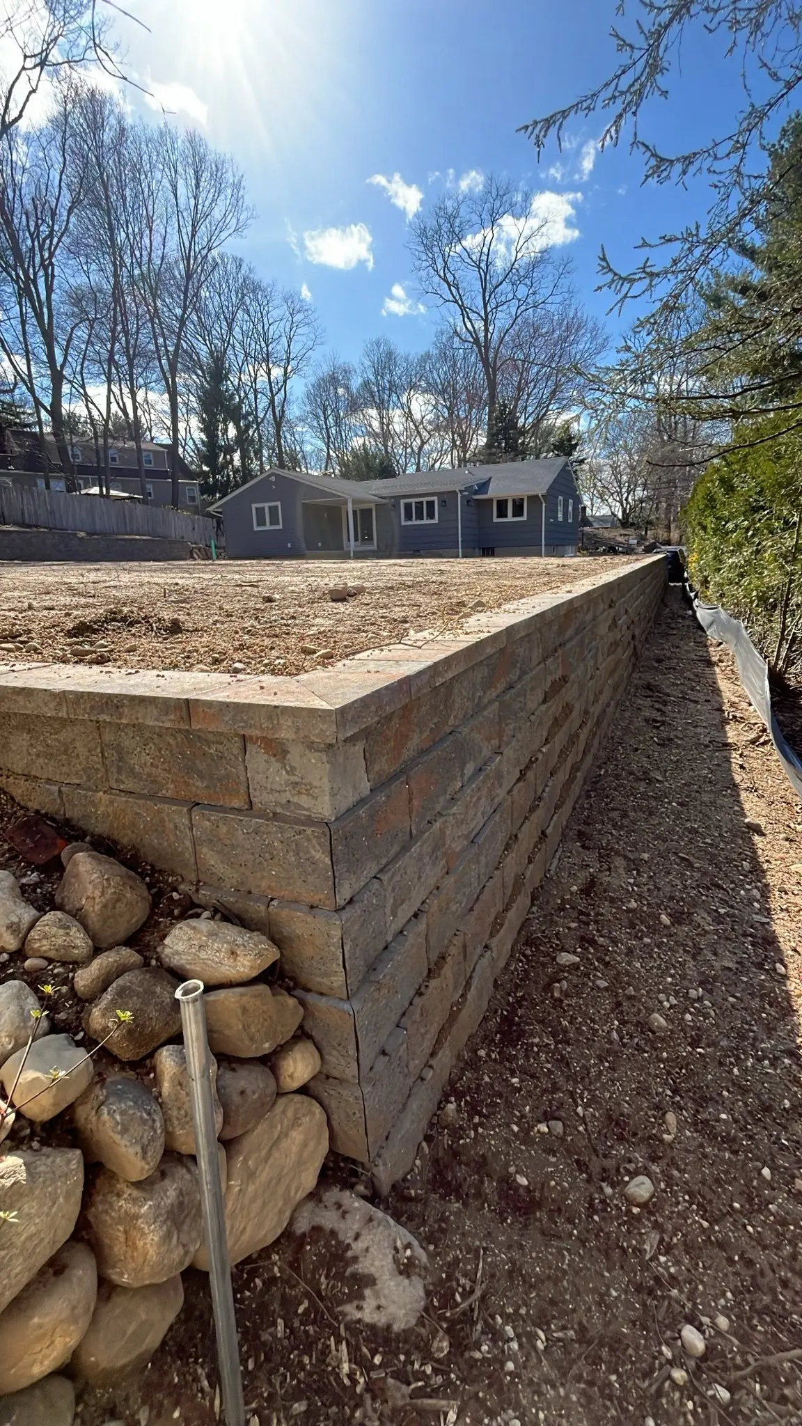Stacked stone retaining wall holding back a graded yard under a dramatic sky