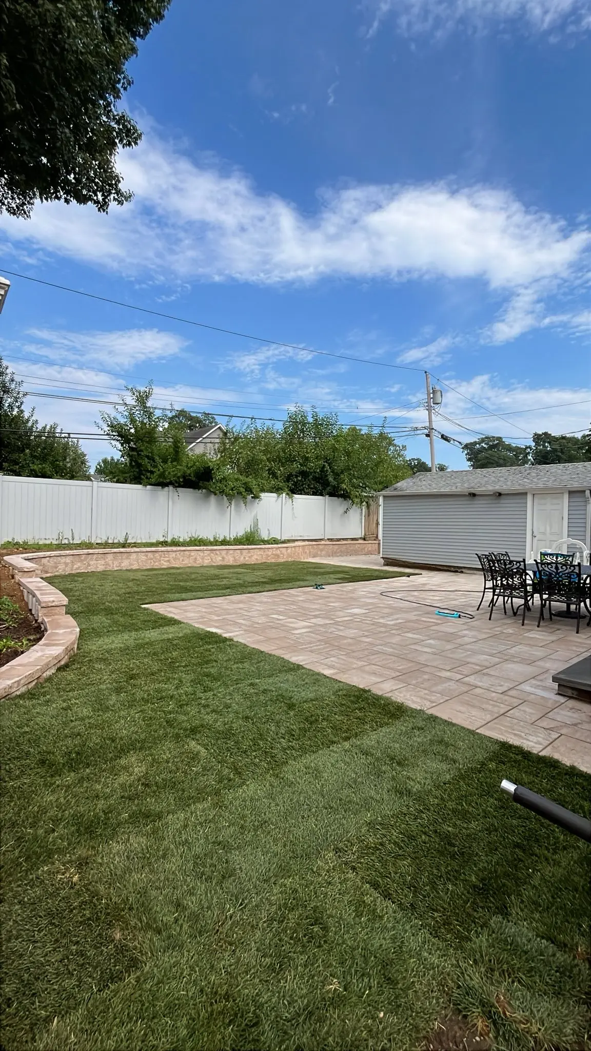 Backyard paver patio and fresh sod lawn with stone border wall